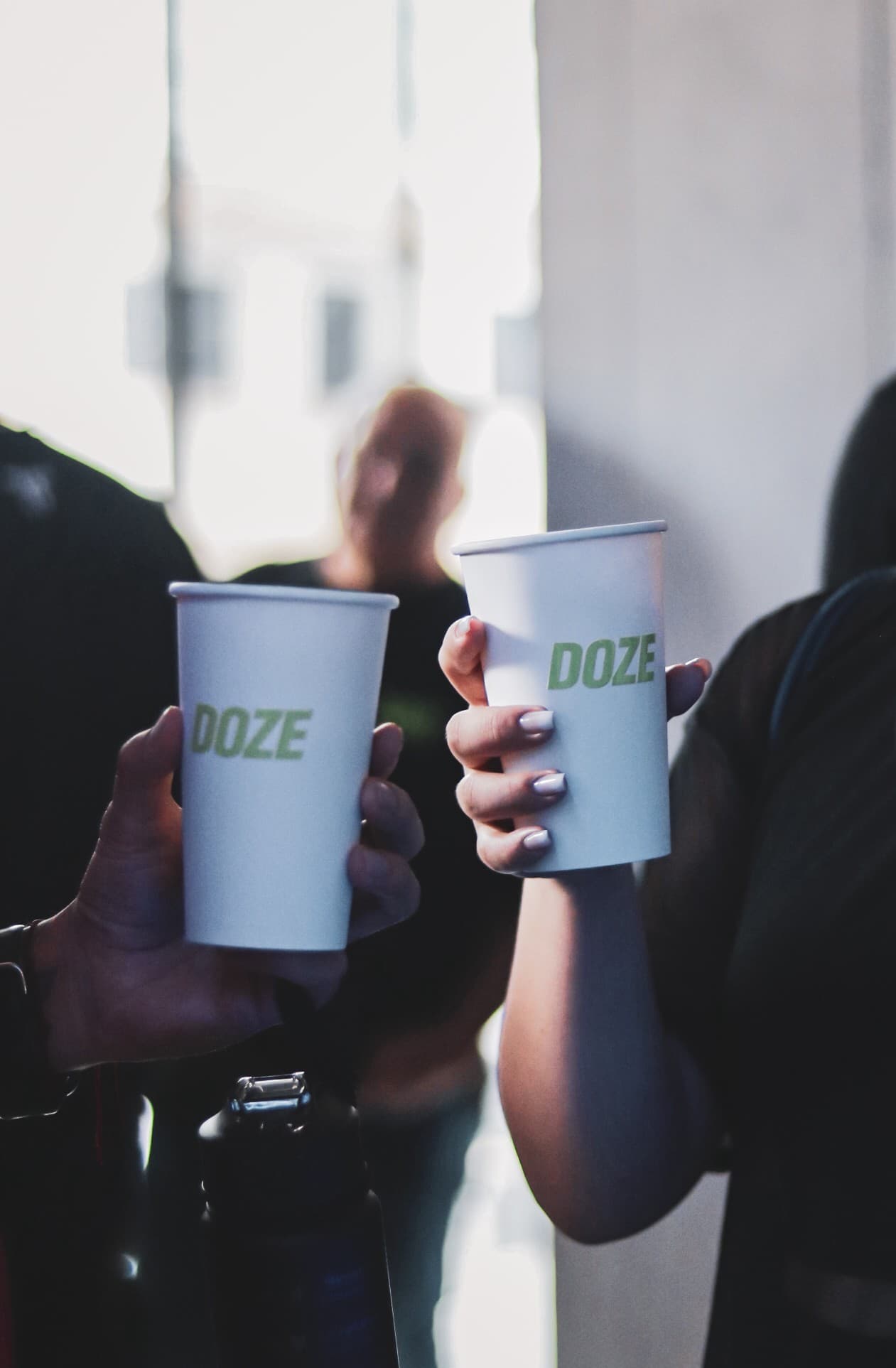 Dos manos brindando con vasos blancos de DOZE