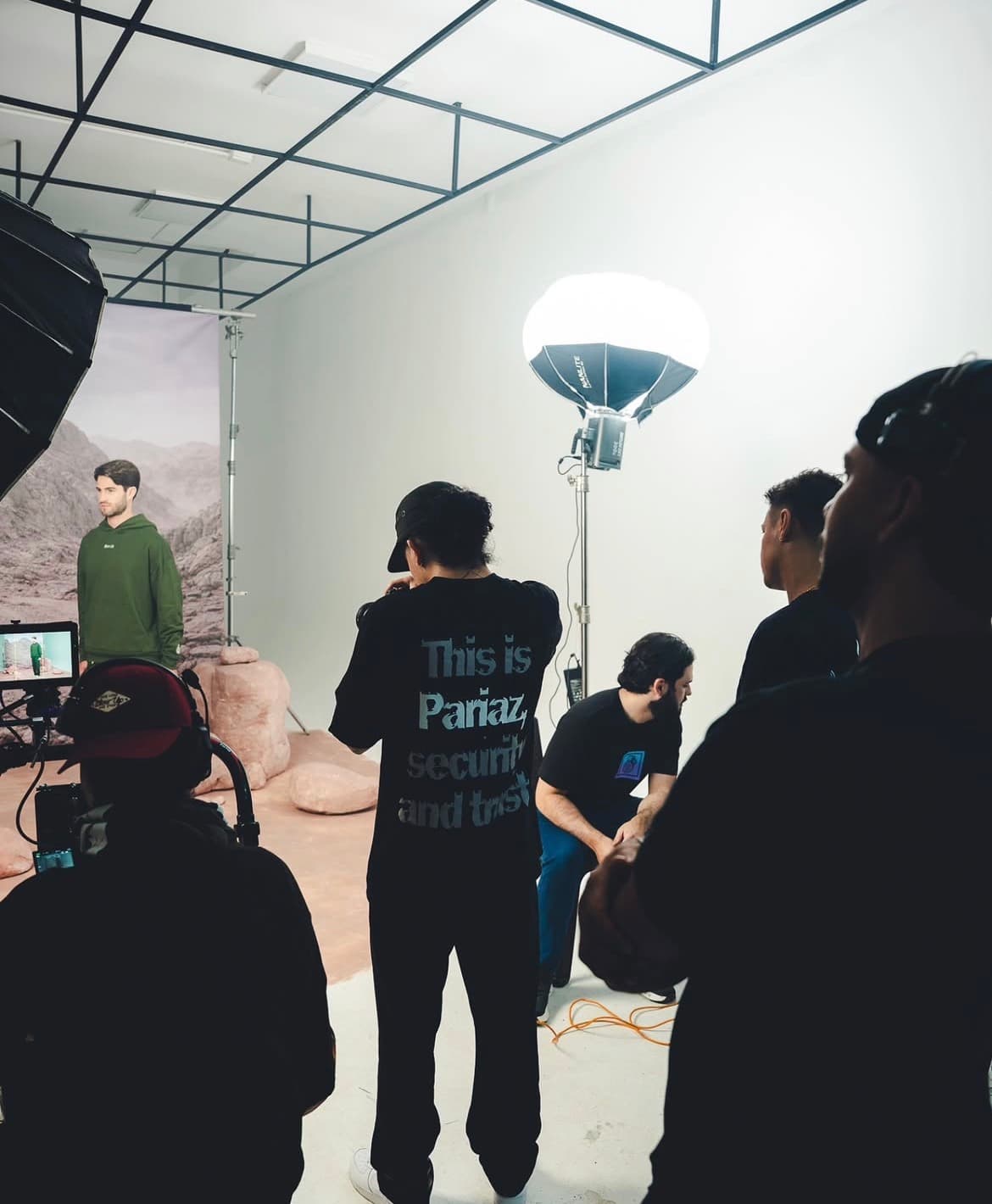 Equipo en set con globo de luz y modelo con hoodie verde frente al telón de montañas